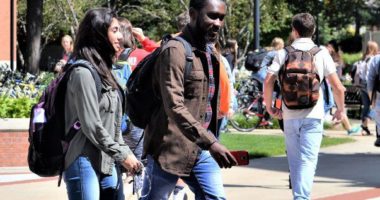 Diverse male and female students walking on a college campus with backpacks