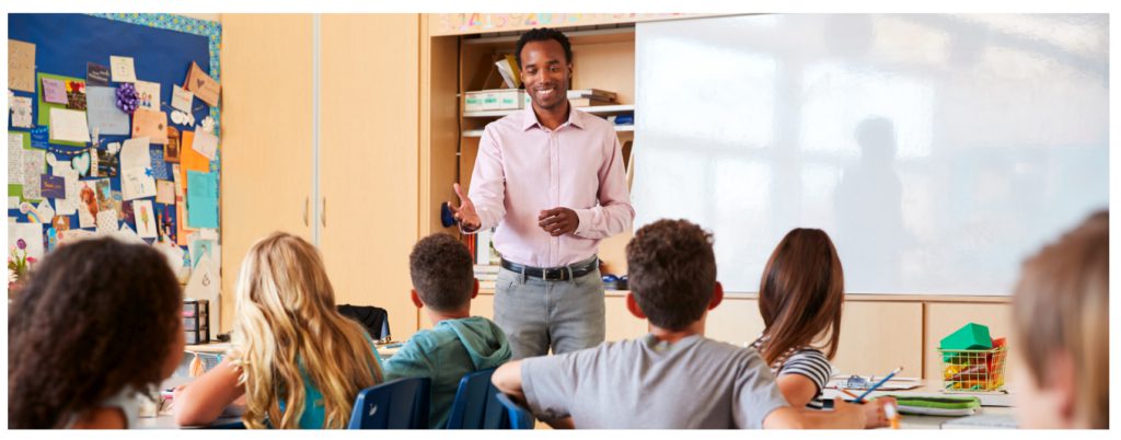 Black male teacher in front of the classroom instructing elementary students