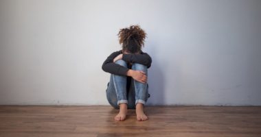 Sad black girl sitting alone on the floor, hugging her knees