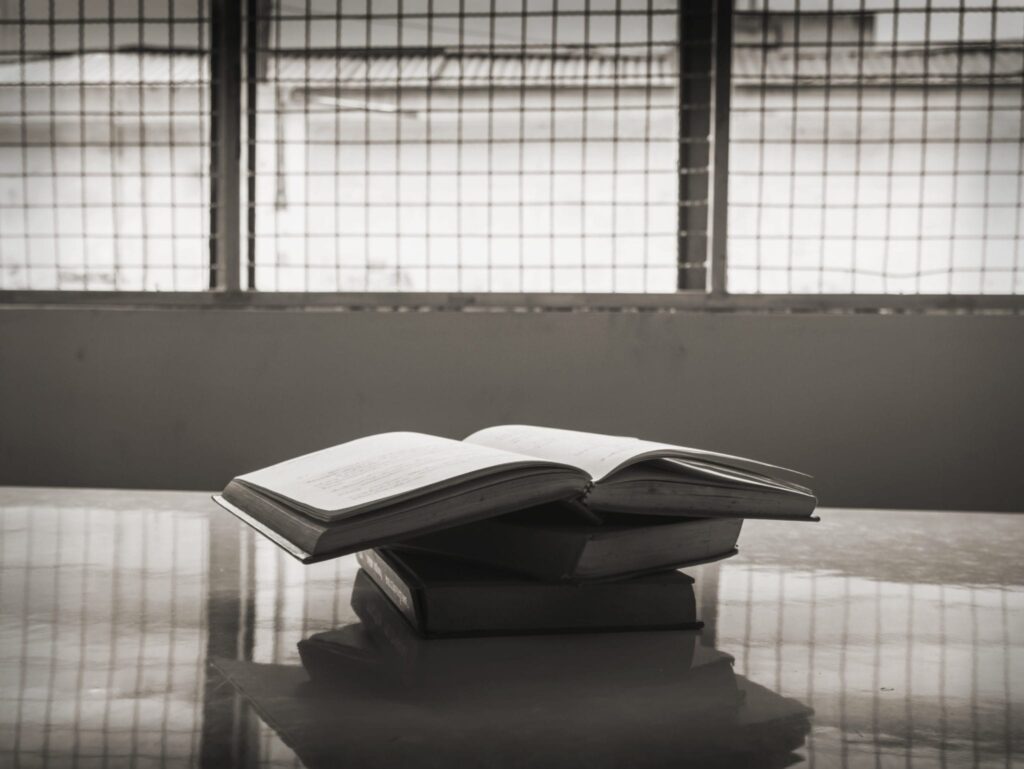 A stack of books on a table with fenced in windows on the background