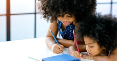 Two cute black girls looking at a book on a desk