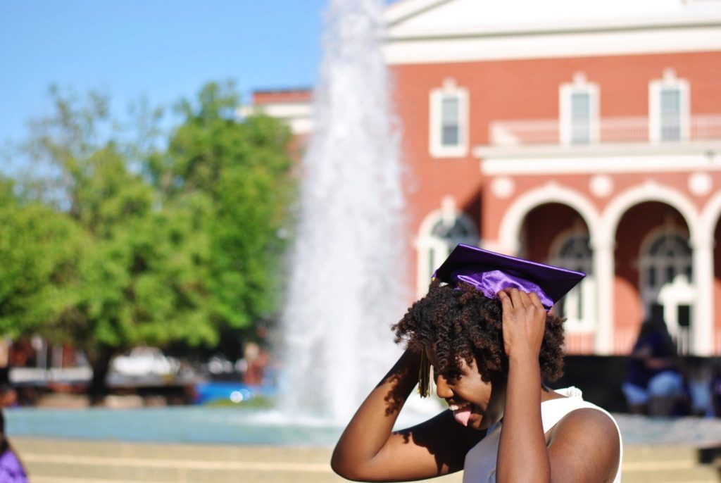 Black girl wearing graduation cap in front of fountain and building