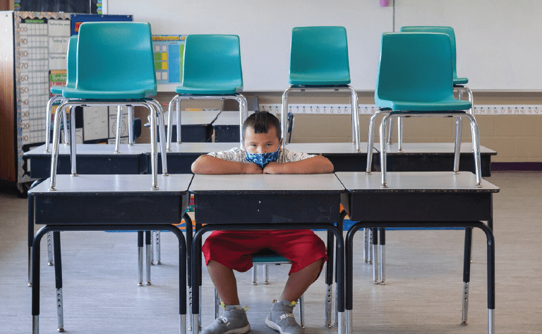 Male student sitting alone in classroom with mask on