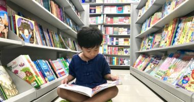 Male child sitting Indian style in library aisle and reading a book