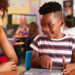 Black female teacher assisting a black male elementary student in classroom