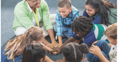 Teacher and students sitting on the floor together stacking hands