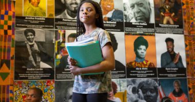 Black female student holding books in front of posters of African Americans