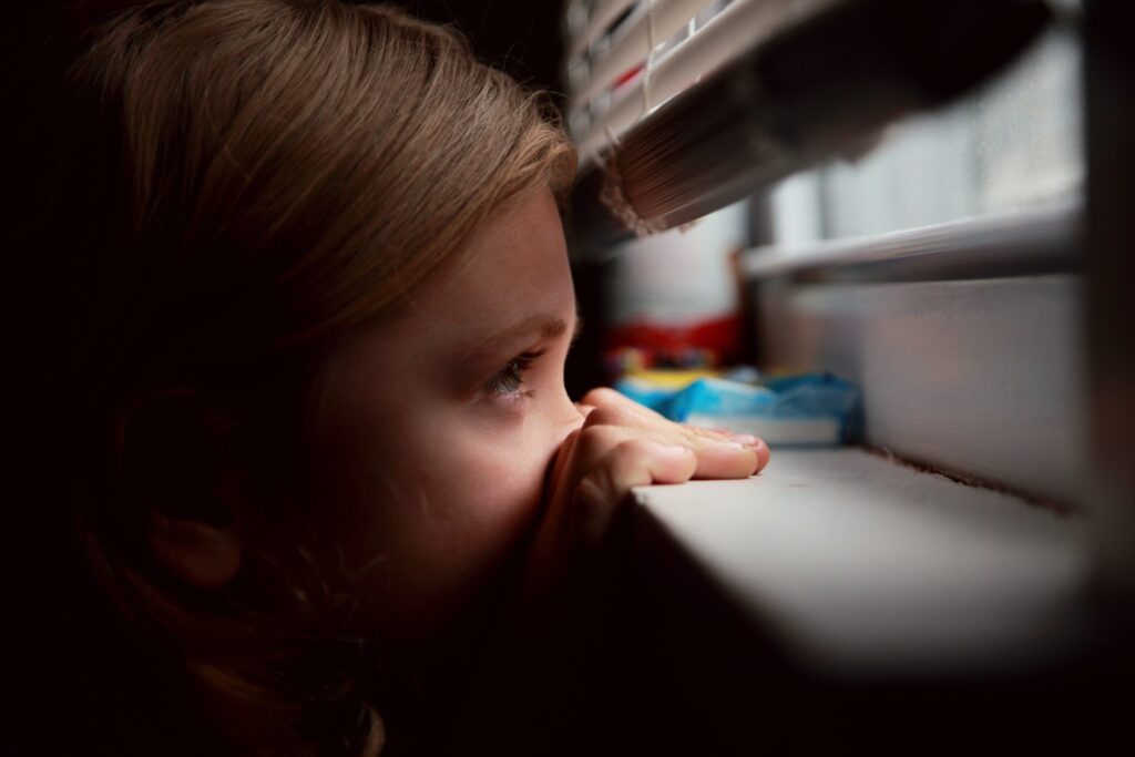 Young girl peeking through window blinds