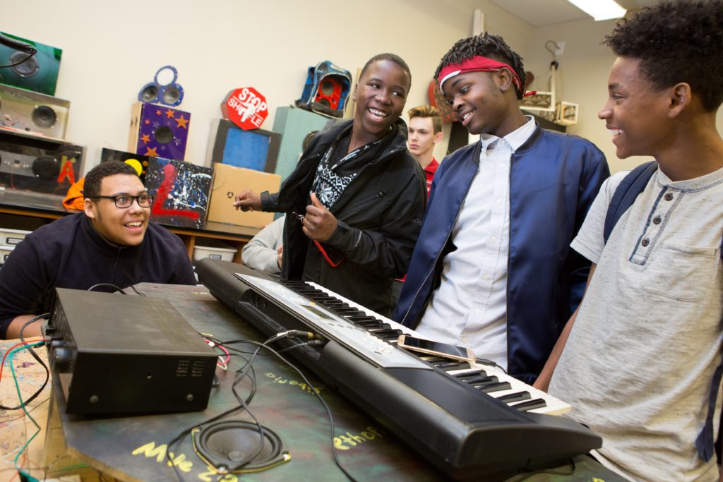 Group of high school male students standing around a keyboard and smiling