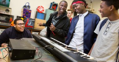 Group of high school male students standing around a keyboard and smiling