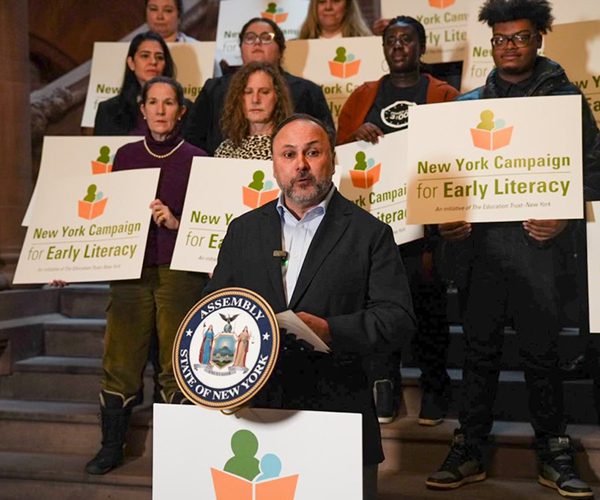 Jeff Smink at a podium with people with signs behind him