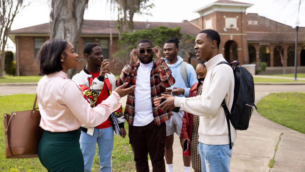 Group of Black students talking together on a path near a building on a college campus.