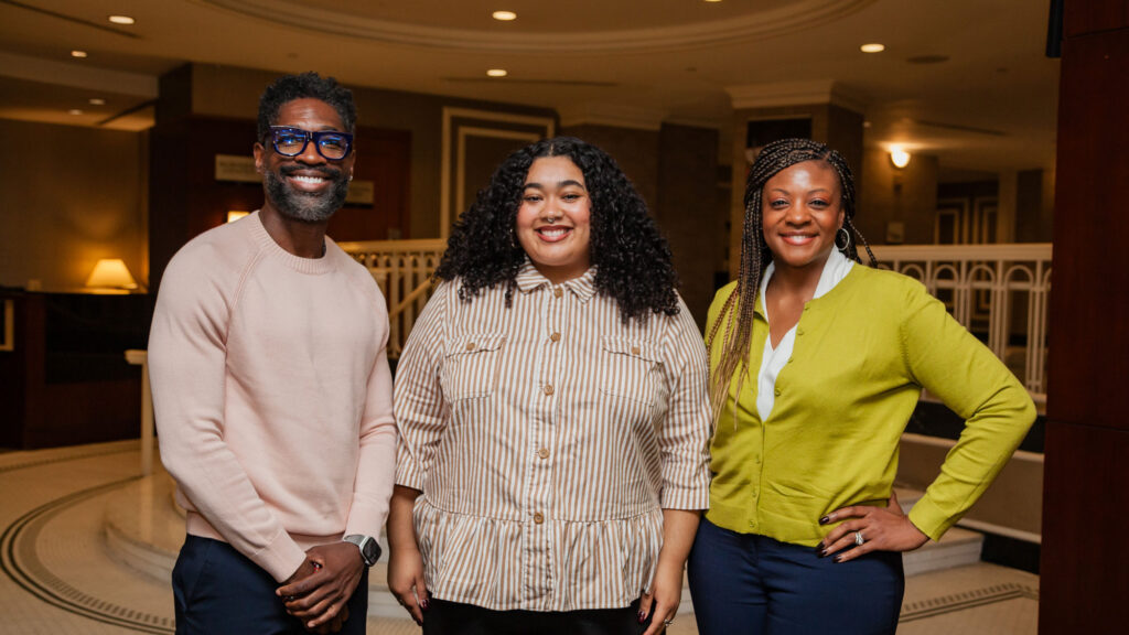 Three people standing -- one man and two women -- smiling at the camera