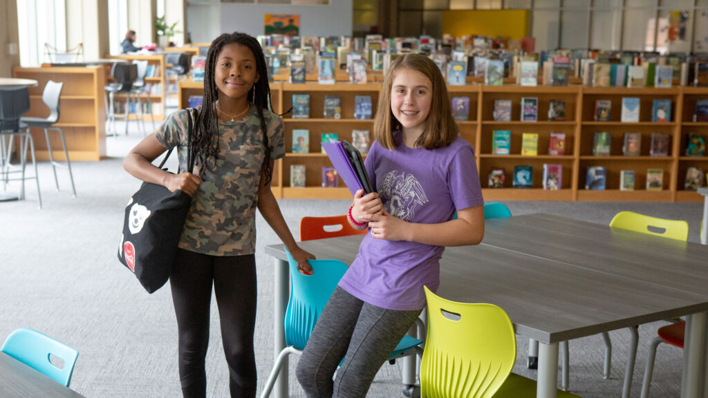 Two seventh-grade students pose for a photo with their notebooks in the library